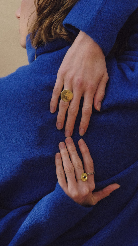 Dos manos sobre un pulover azul llevando tres anillos color oro 
