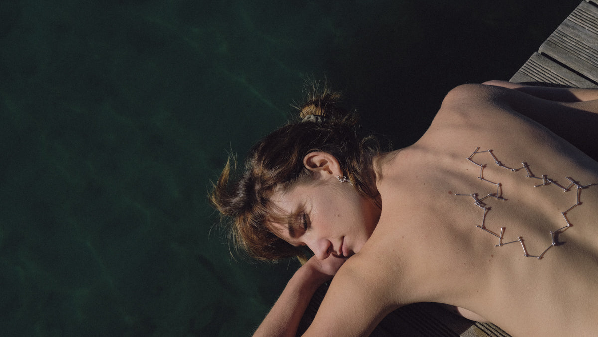 Mujer tumbada en el suelo al lado del mar con el collar constel.lacions y pendientes pluja
